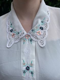 A beautiful vintage shirt with embroidered floral detail in the collar and to the front of the shirt. The shirt is button up down the centre and has short sleeves. It is an off-white to grey colour and slightly sheer. Overall excellent vintage condition with no obvious flaws or issues.  Shirt shown on size 10 model with 32D bust, I would say it is roughly a size 10 UK. When laid flat for the back it is approximately 50cm down, not including the collar. The sleeves are about 23cm long at their longest point (the top) when laid flat.  There are also small slits on the back of the shirt which is part of the design, shown in the last photo. Summer Floral Embroidery Doll Collar Blouse, Summer Blouse With Floral Embroidery And Doll Collar, Floral Embroidery Doll Collar Blouse For Summer, Floral Embroidered Doll Collar Blouse For Summer, Spring Embroidered Blouse With Peter Pan Collar, Embroidered Shirt With Collared Neckline For Spring, Summer Blouse With Peter Pan Lace Collar, Spring Embroidered Blouse With Collared Neckline, Spring Tops With Floral Embroidery And Collared Neckline