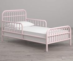 a pink metal bed sitting on top of a wooden floor next to a white wall