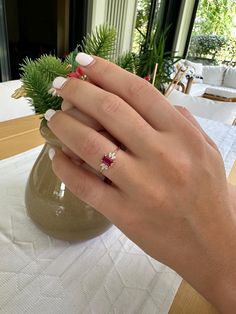 a woman's hand with a ring on it and a plant in the background