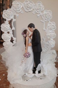 a wedding cake topper with a bride and groom in front of a white rose arch