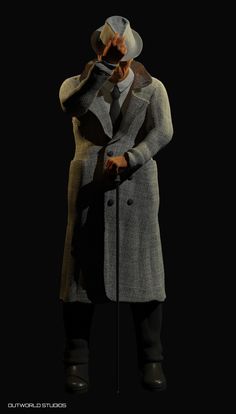 a man in a gray coat and hat is holding a microphone to his face while standing on a black background