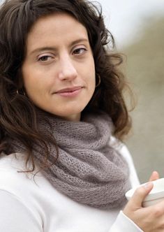 a woman wearing a gray scarf and holding a cup in her hand while looking at the camera