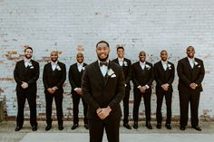 a group of men standing next to each other in front of a white brick wall