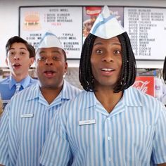 three men in blue shirts and white hats are standing next to each other with food on their heads