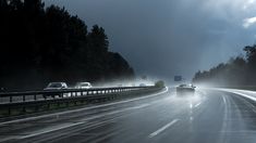 cars driving on a highway in the rain and fog with dark clouds above them at night