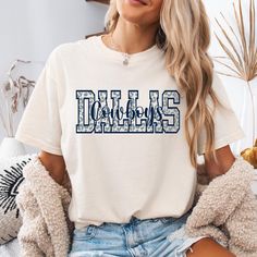 a woman wearing a white shirt with the word dallas in blue letters on it sitting down