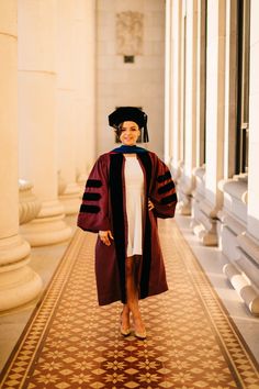 a woman in a graduation gown and cap is walking down the hall with her hand on her hip