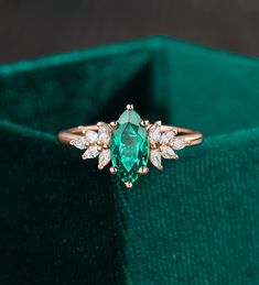 an emerald colored ring with white diamonds on it in a green velvet box, close up