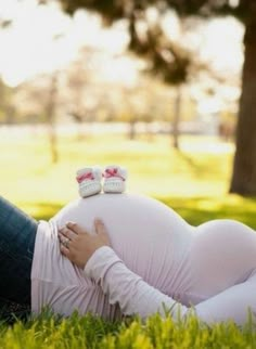 a pregnant woman laying in the grass with her baby shoes on top of her belly