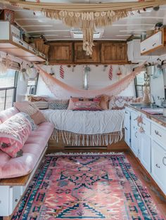 the inside of a camper with pink and white decor on the bed, rugs, cabinets and drawers