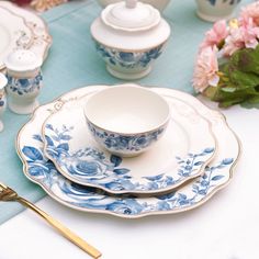 a blue and white china set on a table with pink flowers in the vases