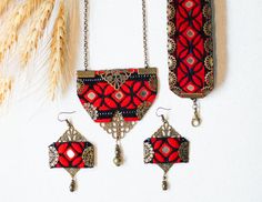 three pieces of jewelry hanging from chains on a white wall next to a wheat plant