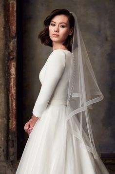 a woman wearing a white wedding dress with a long veil on her head and shoulder