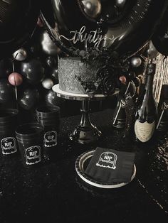 a black and silver party with balloons, cake, wine bottles and napkins on the table