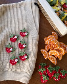 some fruit is laying on the floor next to a sweater and other items that include strawberries, oranges, and lemons