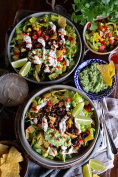 three bowls filled with different types of food on top of a wooden table next to chips and guacamole