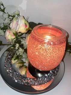 an orange candle sits on a black plate next to flowers and a vase with white roses