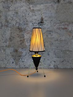 a lamp that is sitting on a table next to a stone wall with a cord running through it