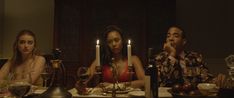 three people sitting at a dinner table with candles in front of them and one person standing up