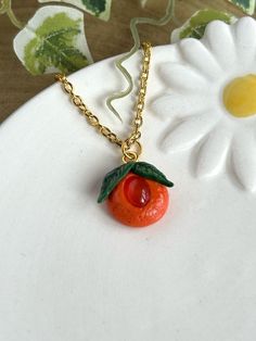 A magical handmade orange fruit pendant with a carnelian crystal. Sculpted with polymer clay, this dainty glossy orange has the fruit texture and painted green leaves with a warm orange carnelian in the centre.  This pendant comes with a 22" gold chain.  Carnelian is a orange crystal part of the chalcedony family. It's a stone that's said to enhance your motivation and creativity. Its known for bringing strength, courage and warmth, aswell as encouraging personal inner growth. If you have any qu Handmade Orange Resin Necklace, Orange Pendant Charm Necklaces For Gifts, Unique Orange Resin Jewelry, Handmade Orange Charm Necklace As A Gift, Handmade Orange Charm Necklace For Gift, Orange Polymer Clay Jewelry As A Gift, Orange Jewelry With Fruit Design For Gifts, Orange Fruit Design Jewelry Gift, Orange Fruit Design Jewelry For Gift