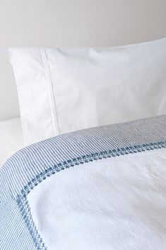 a close up of a bed with white sheets and blue trimmings on it