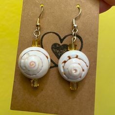 a pair of earrings with shells hanging from it's earwires in front of a heart