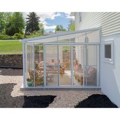 a white house with glass walls and patio furniture in the back yard, surrounded by gravel