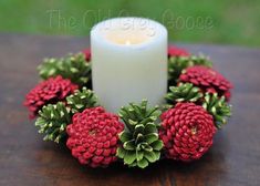 a white candle sitting on top of a wooden table next to red flowers and greenery