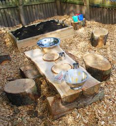 an outdoor table made out of wood logs and bowls on top of it in the middle of a yard