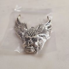 a silver skull with wings on it's head in a plastic bag, sitting on top of a table