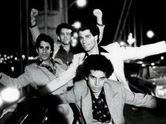 black and white photograph of men in suits on the street at night with their arms up