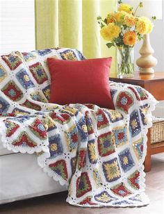 a crocheted afghan sits on a couch next to a vase with yellow flowers