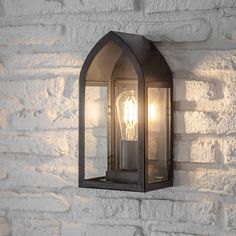 an outdoor light mounted on the side of a white brick wall with a clear glass shade