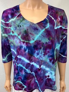 Ice tie dye 2X size women's tee shirt. This tee is a medium weight tee, and 100% cotton, has a natural stretch to it. Is easy care machine wash and dry with dark colors. This tee has 3/4 sleeves and a V-neckline. Peacock colors, blue, green & purple. The tee is comfy and not form fitting, will hang loose. Comfy and wears and washes well. Measurements are garment laid out flat  24 inches from armpit to armpit across the front  25 inches from shoulder near neckline, down front to bottom hem 11 inches from armpit to sleeve hem down sleeve bottom Summer Acid Wash V-neck Top, Ice Tie Dye, Peacock Colors, Hang Loose, V Neck Tee, Dark Colors, 11 Inches, Green And Purple, Medium Weight