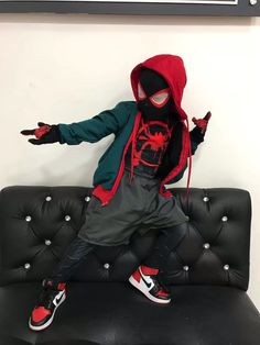 a young boy in a spiderman costume sitting on a black couch with his arms outstretched