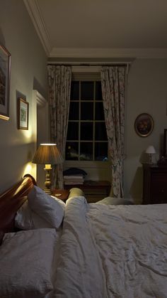 a bed with white sheets and pillows in a bedroom next to a window at night