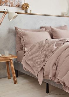 a bed with pink sheets and pillows in a room next to a wooden side table