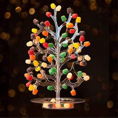 a tree made out of gummy bears sitting on top of a cake plate with lights in the background