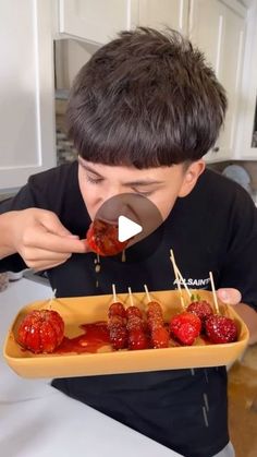 a young boy is eating strawberries with toothpicks in a tray on the kitchen counter