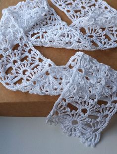 two white crocheted scarves sitting on top of a cutting board