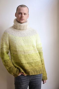 a man standing in front of a white wall wearing a yellow sweater and black jeans