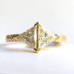 a yellow gold engagement ring with a princess cut diamond in the center, on a white surface