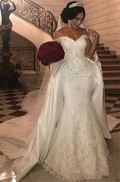 a woman in a white wedding dress standing on the stairs with her hands behind her back