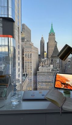 a desk with a computer monitor and book on it in front of a cityscape