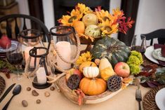 a centerpiece with pumpkins, gourds and other autumn decorations sits on a dining room table