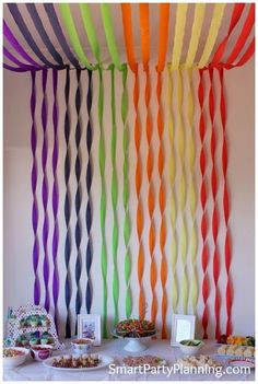 rainbow streamers are hanging from the ceiling in front of a table with desserts