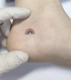 a small rainbow tattoo on the left side of the foot, with a doctor's glove holding it