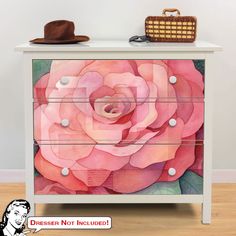 a white dresser with a pink flower painted on it's side and a brown hat sitting on top