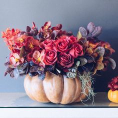 an arrangement of flowers in a pumpkin shaped vase on a table next to two small pumpkins