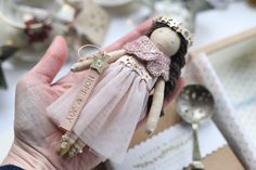 a hand holding a small doll with a tag on it's chest and spoons in the background